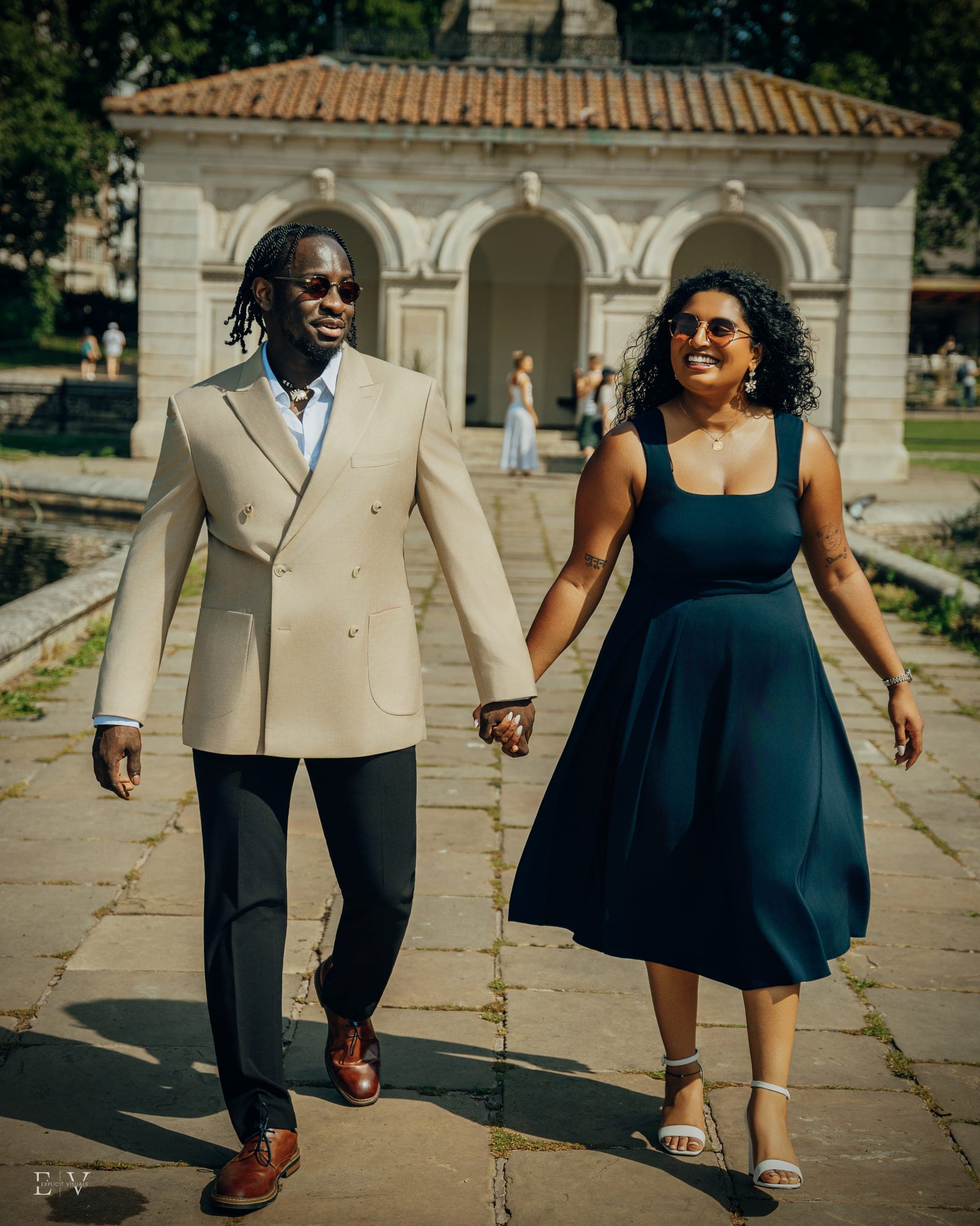 Mid-stride on the same path, hands linked and both turned to look at each other.
