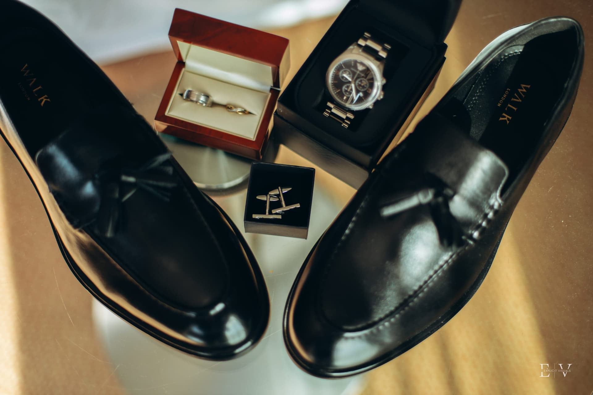 The groom's things laid out before the day — black tassel loafers either side of a wooden ring box, a steel watch and a pair of cufflinks.
