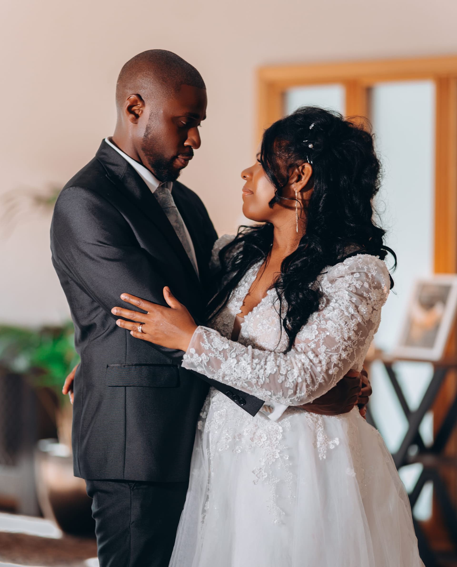 The couple stand face to face indoors, her hand flat on his chest, both looking down.