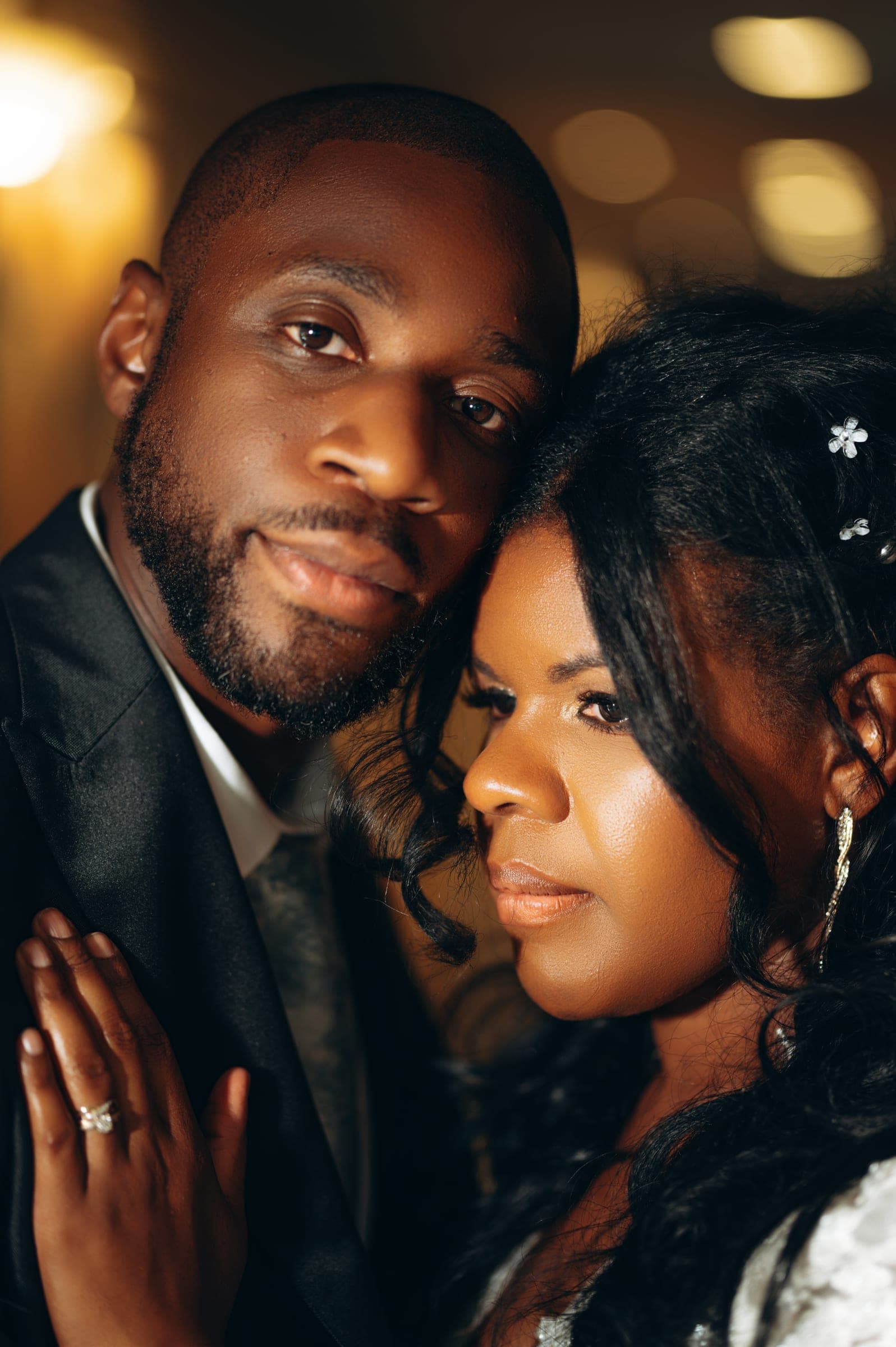 A close portrait of the two of them cheek to cheek, her engagement ring catching the warm light.