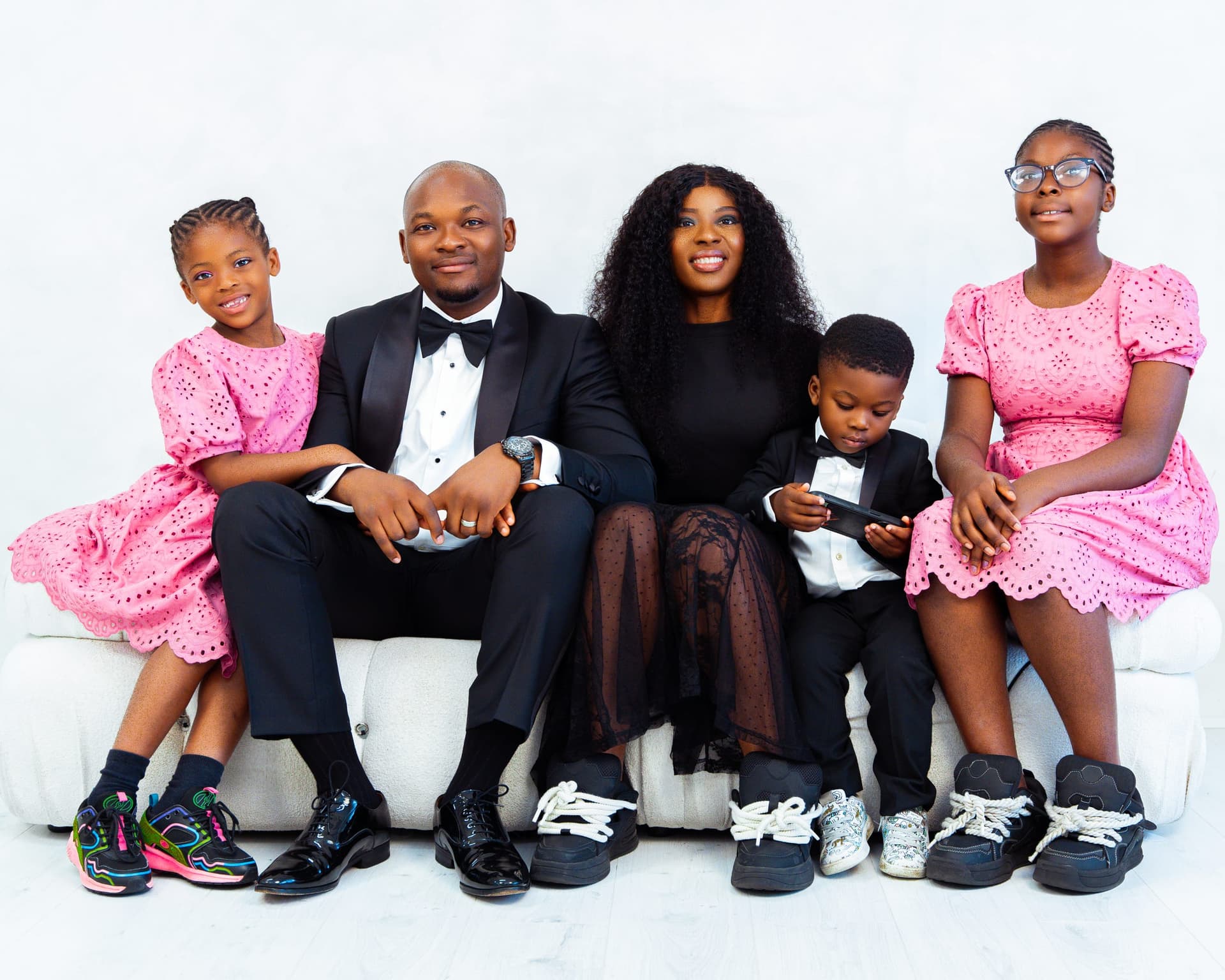 The whole family of five along a white sofa — two daughters in pink either end, their son in a small tuxedo, the parents at the centre.