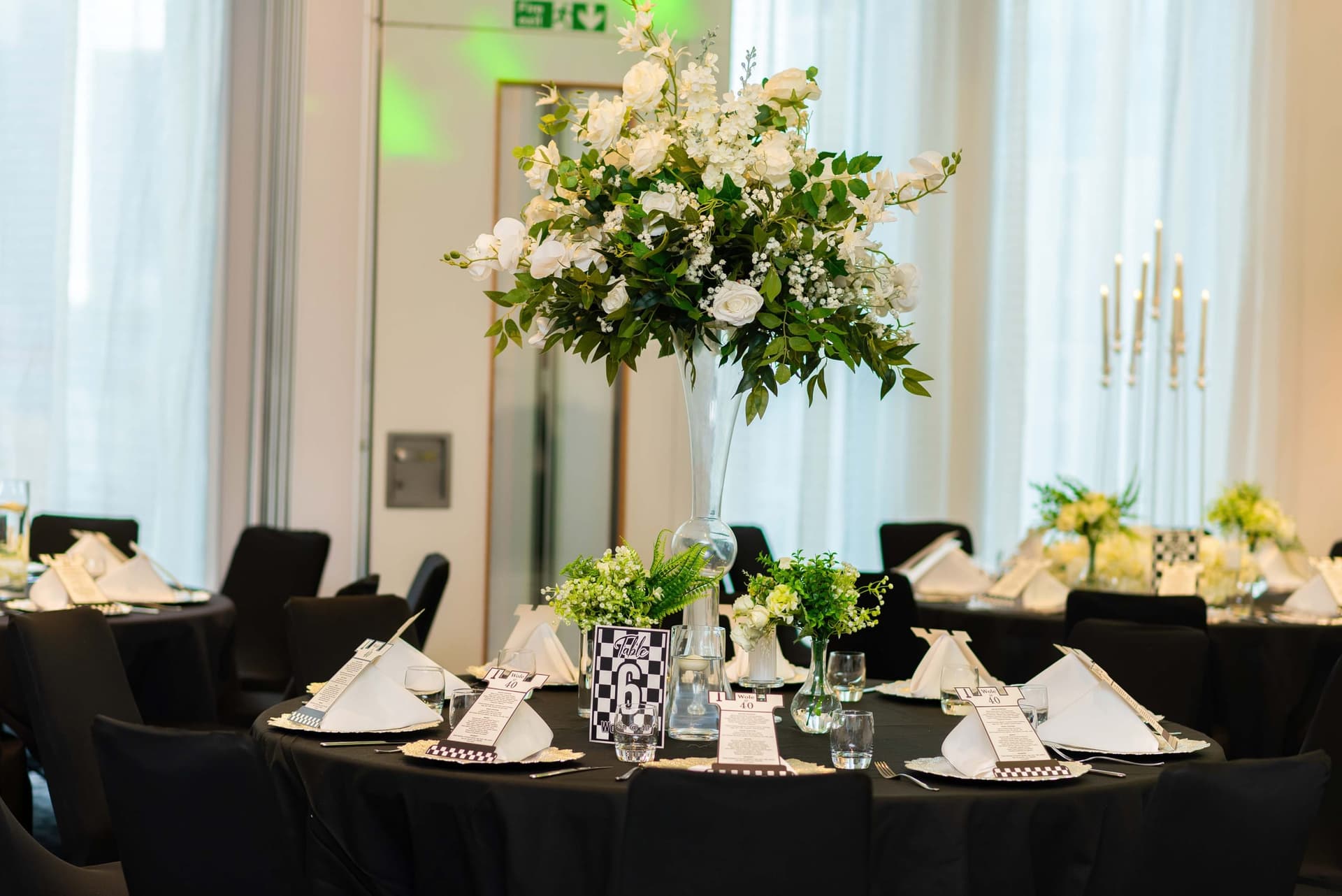 The same arrangement at eye level, white roses and greenery raised on a glass column above the place settings.